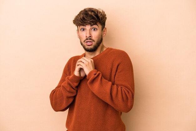 Joven árabe aislado sobre fondo beige asustado y asustado.