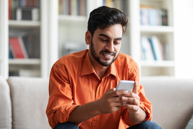 Un joven árabe feliz descansando en casa usando un teléfono celular