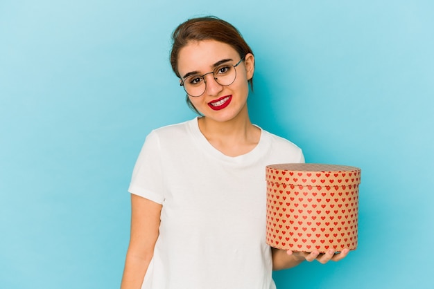 Joven árabe flaca sosteniendo una caja de San Valentín feliz, sonriente y alegre.