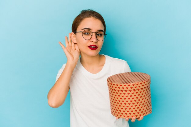 Joven árabe flaca sosteniendo una caja de San Valentín tratando de escuchar un chisme.