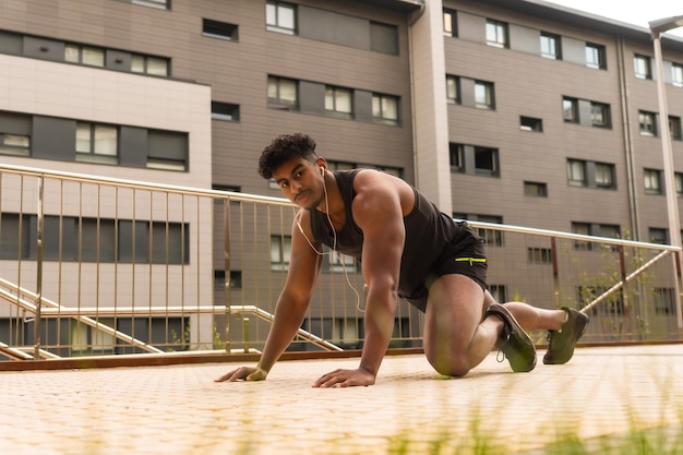 Joven árabe fuerte haciendo deportes en la ciudad haciendo flexiones y mirando a la cámara