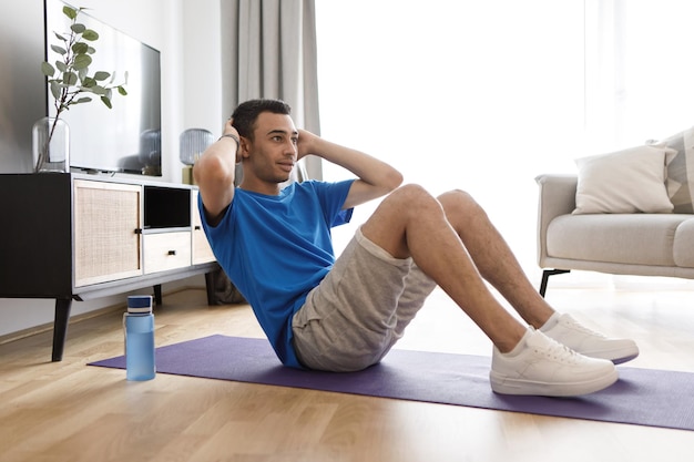 Joven árabe haciendo ejercicio en una estera de yoga fortaleciendo los músculos abdominales durante el espacio libre de entrenamiento doméstico