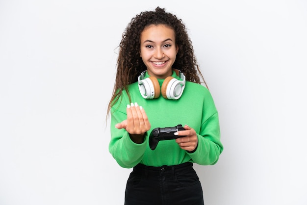 Joven árabe jugando con un controlador de videojuegos aislado de fondo blanco invitando a venir con la mano Feliz de que hayas venido