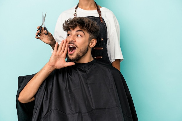 Joven árabe listo para cortarse el pelo aislado sobre fondo azul gritando y sosteniendo la palma cerca de la boca abierta.