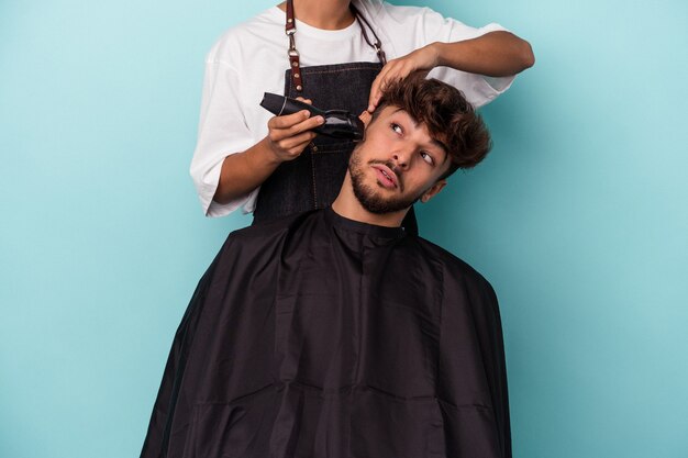 Joven árabe listo para cortarse el pelo aislado sobre fondo azul.