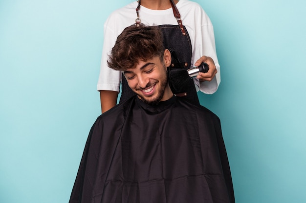 Joven árabe listo para cortarse el pelo aislado sobre fondo azul.