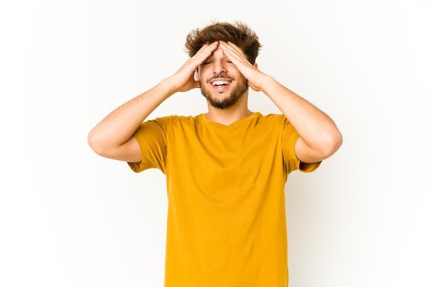 Joven árabe en la pared blanca se ríe con alegría manteniendo las manos en la cabeza. Concepto de felicidad.