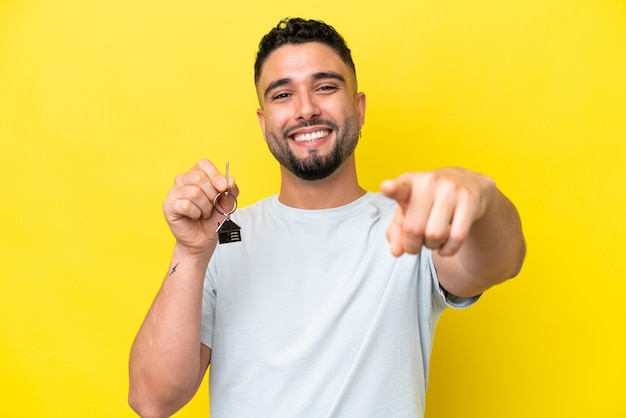 Un joven árabe que sostiene las llaves de casa aisladas en un fondo amarillo te señala con una expresión de confianza