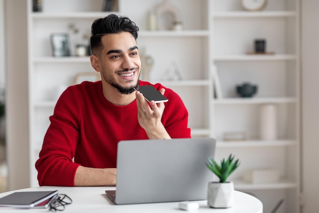 Joven árabe que usa un teléfono inteligente para grabar mensajes de voz en casa