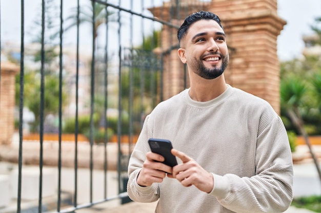 Un joven árabe sonriendo con confianza usando su teléfono inteligente en la calle