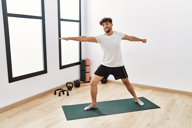 Joven árabe sonriendo seguro entrenando yoga en el centro deportivo