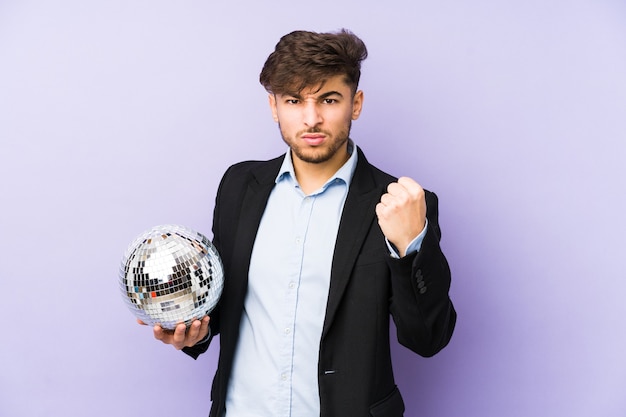 Joven árabe sosteniendo un balón de fiesta aislado mostrando puño, expresión facial agresiva.