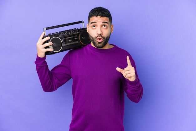 Joven árabe sosteniendo un cassette de radio aislado Joven árabe escuchando música apuntando al revés con la boca abierta.