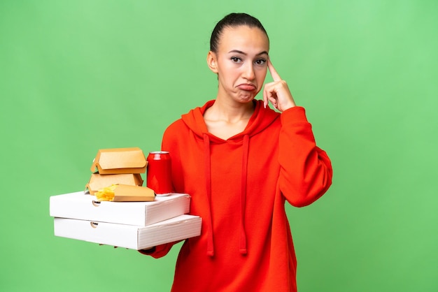 Joven árabe sosteniendo comida rápida sobre un fondo aislado pensando en una idea