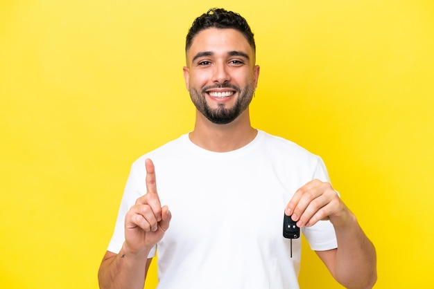 Joven árabe sosteniendo las llaves del auto aislado en un fondo amarillo señalando una gran idea