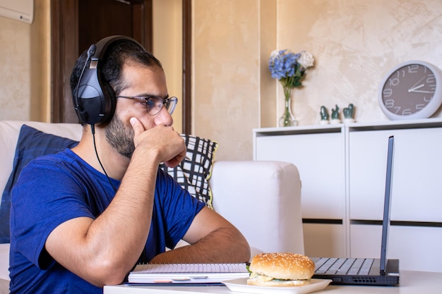 Joven árabe trabajando en casa con laptop y papeles en el escritorio