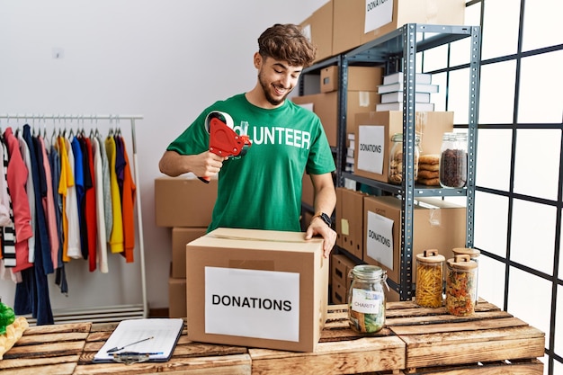 Joven árabe con uniforme de voluntario empacando una caja de donaciones en el centro de caridad