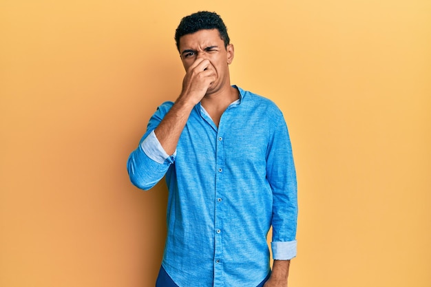 Joven árabe vestido con ropa informal que huele algo apestoso y repugnante olor intolerable aguantando la respiración con los dedos en la nariz mal olor