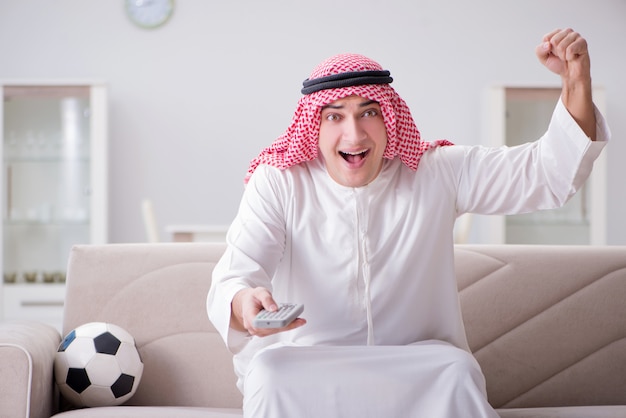 Joven árabe viendo fútbol sentado en el sofá
