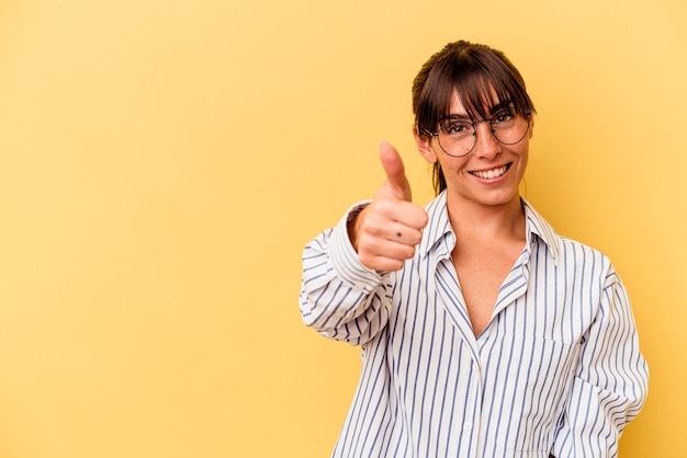 Joven argentina aislada de fondo amarillo sonriendo y levantando el pulgar