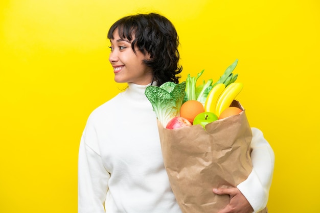 Foto joven argentina sosteniendo una bolsa de compras aislada de fondo amarillo mirando hacia el lado