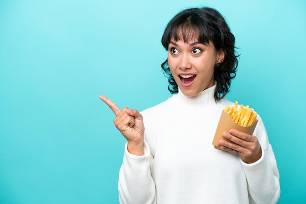 Joven argentina sosteniendo papas fritas aisladas de fondo azul con la intención de darse cuenta de la solución mientras levanta un dedo