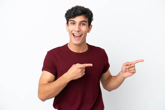 Joven argentino aislado de fondo blanco sorprendido y apuntando hacia el lado