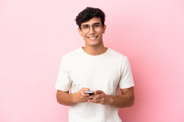 Joven argentino aislado de fondo rosa enviando un mensaje con el móvil