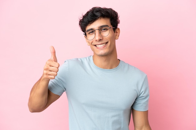 Joven argentino aislado de fondo rosa con gafas y con el pulgar hacia arriba