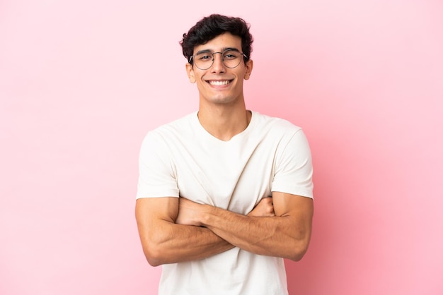 Joven argentino aislado de fondo rosa manteniendo los brazos cruzados en posición frontal