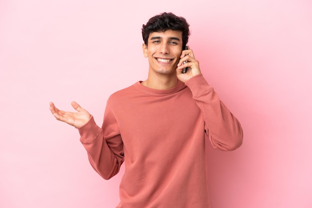 Joven argentino aislado de fondo rosa manteniendo una conversación con el teléfono móvil con alguien