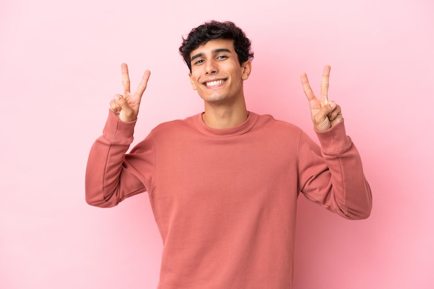 Joven argentino aislado de fondo rosa que muestra el signo de la victoria con ambas manos