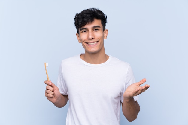 Joven argentino cepillando sus dientes sobre la pared azul aislada con expresión facial sorprendida