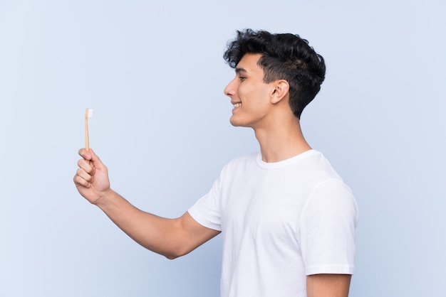 Joven argentino cepillando sus dientes sobre la pared azul aislada con expresión feliz