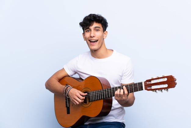 Joven argentino con guitarra sobre pared azul aislado celebrando una victoria