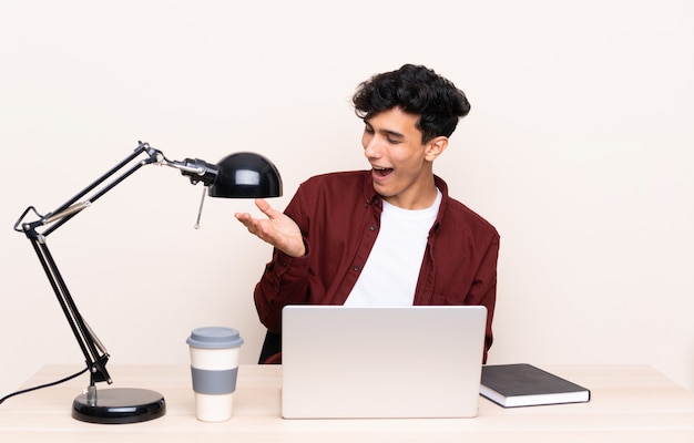 Joven argentino en una mesa con un portátil en su lugar de trabajo con copyspace imaginario en la palma