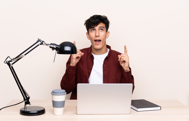 Joven argentino en una mesa con un portátil en su lugar de trabajo señalando con el dedo índice una gran idea