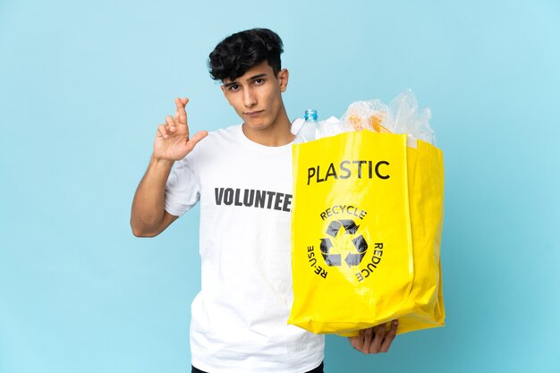 Joven argentino sosteniendo una bolsa llena de plástico con los dedos cruzados y deseando lo mejor