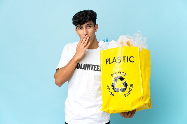 Joven argentino sosteniendo una bolsa llena de plástico feliz y sonriente cubriendo la boca con la mano