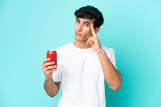 Joven argentino sosteniendo un refresco aislado de fondo azul pensando en una idea