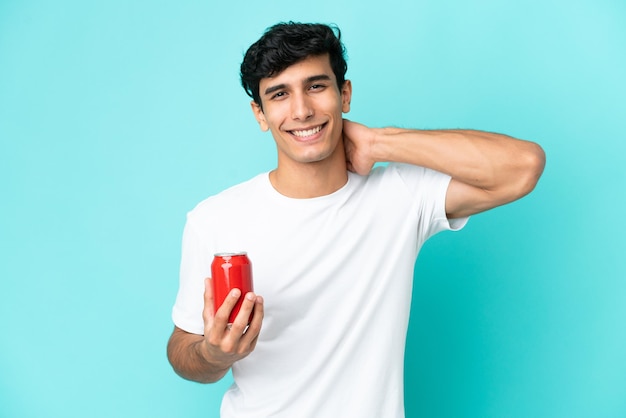 Joven argentino sosteniendo un refresco aislado de fondo azul riendo