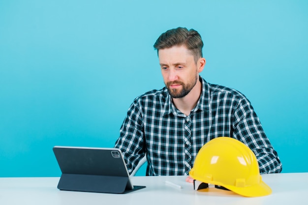 El joven arquitecto está mirando la pantalla de su tableta con fondo azul