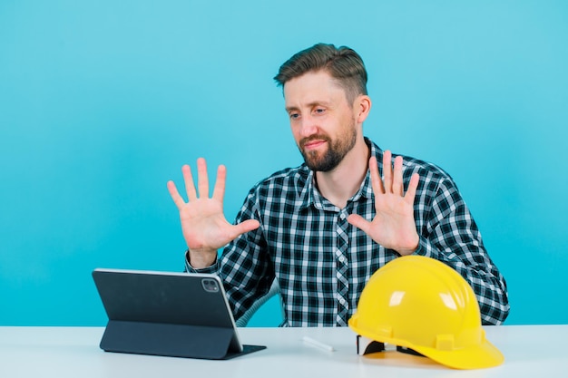 El joven arquitecto está mostrando puñados de gestos al sentarse frente a la tableta con fondo azul.