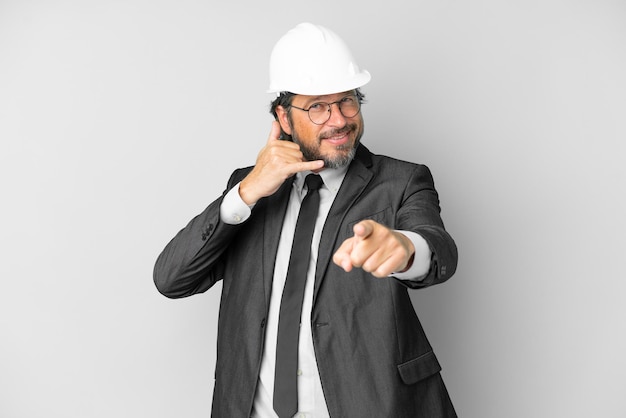 Joven arquitecto hombre con casco sobre fondo aislado haciendo gesto de teléfono y apuntando al frente