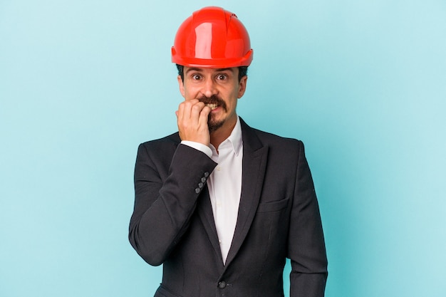 Joven arquitecto hombre caucásico aislado sobre fondo azul mordiéndose las uñas, nervioso y muy ansioso.