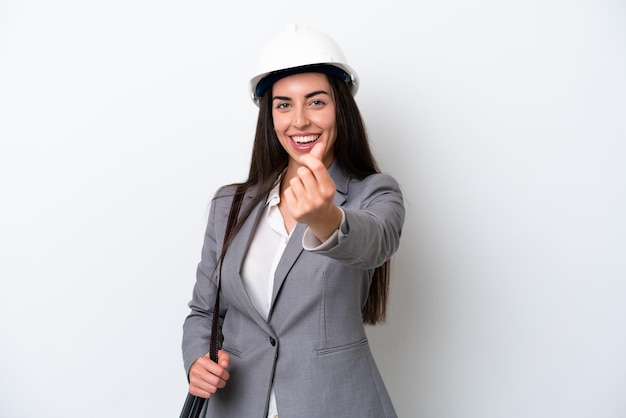 Joven arquitecto mujer caucásica con casco y sosteniendo planos aislados en fondo blanco haciendo gesto de dinero