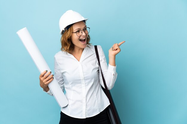 Joven arquitecto mujer georgiana con casco y sosteniendo planos sobre una pared aislada con la intención de darse cuenta de la solución mientras levanta un dedo