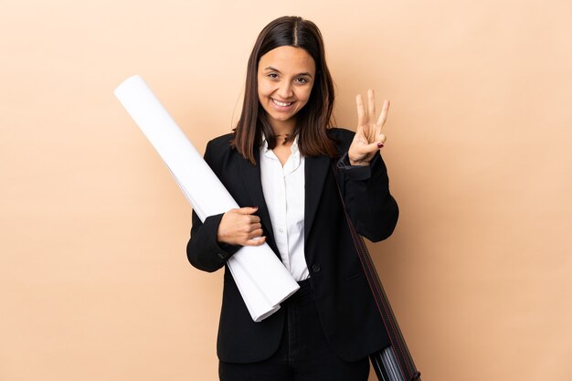 Joven arquitecto mujer sosteniendo planos sobre antecedentes aislados feliz y contando tres con los dedos