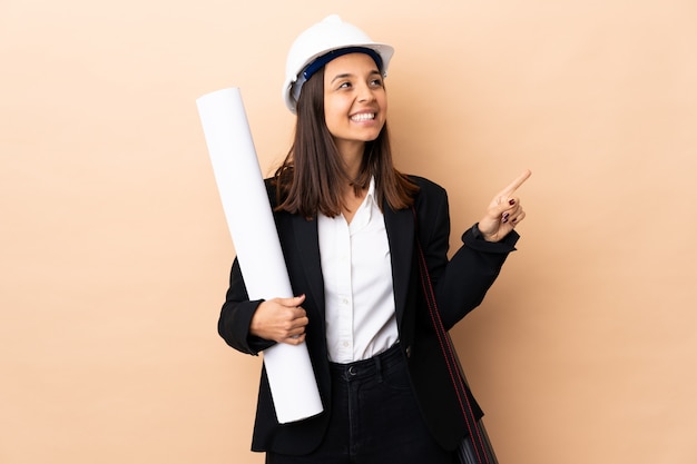 Joven arquitecto mujer sosteniendo planos sobre pared apuntando hacia una gran idea