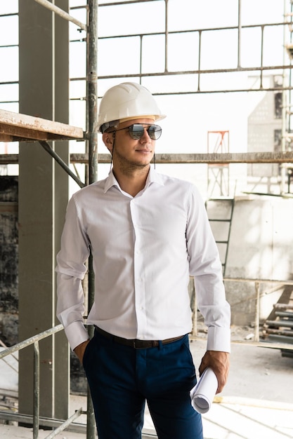 Joven arquitecto o empresario con casco y sosteniendo planos en un sitio en construcción